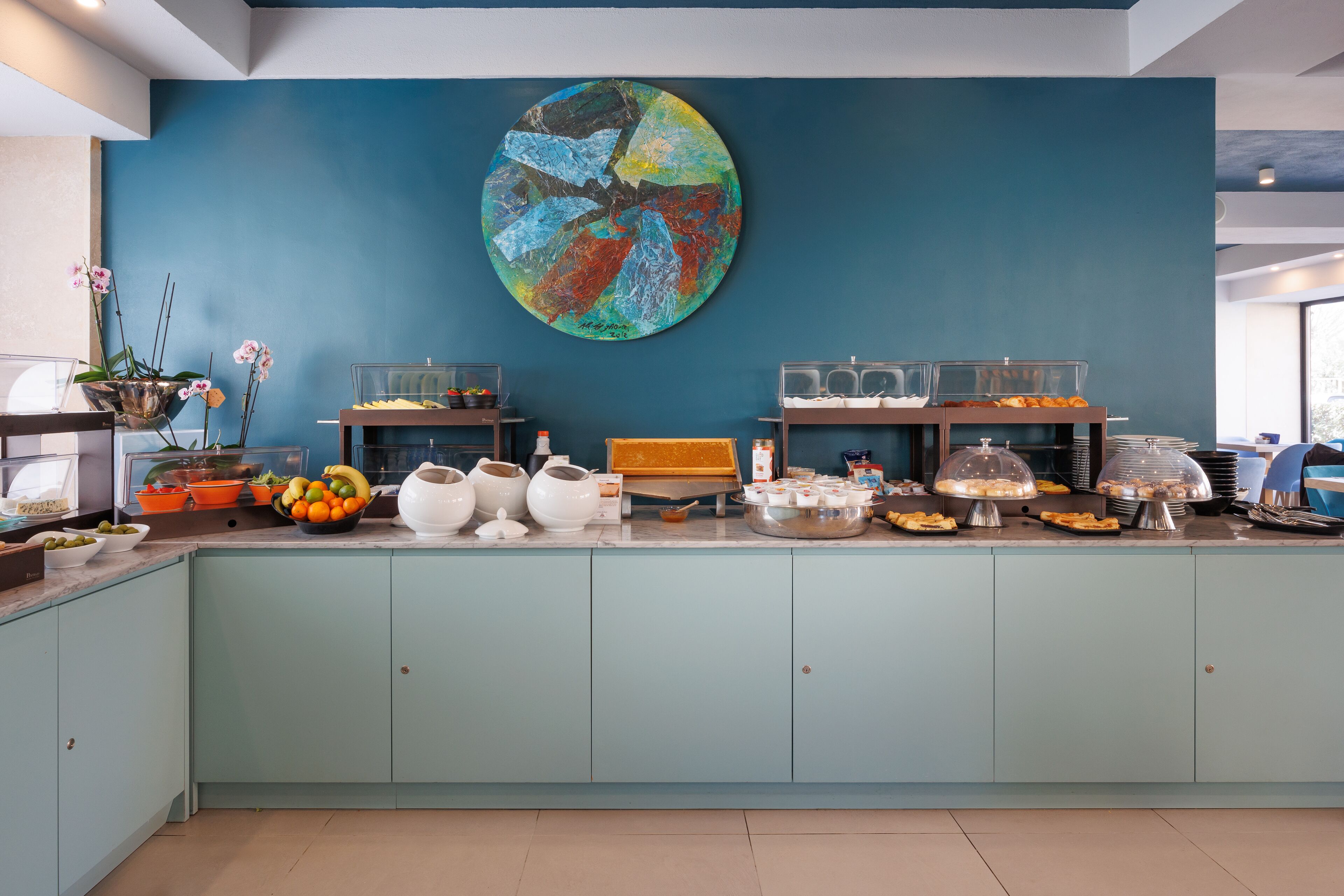 A buffet area with a blue wall, a large abstract painting, and various food and drink items.
