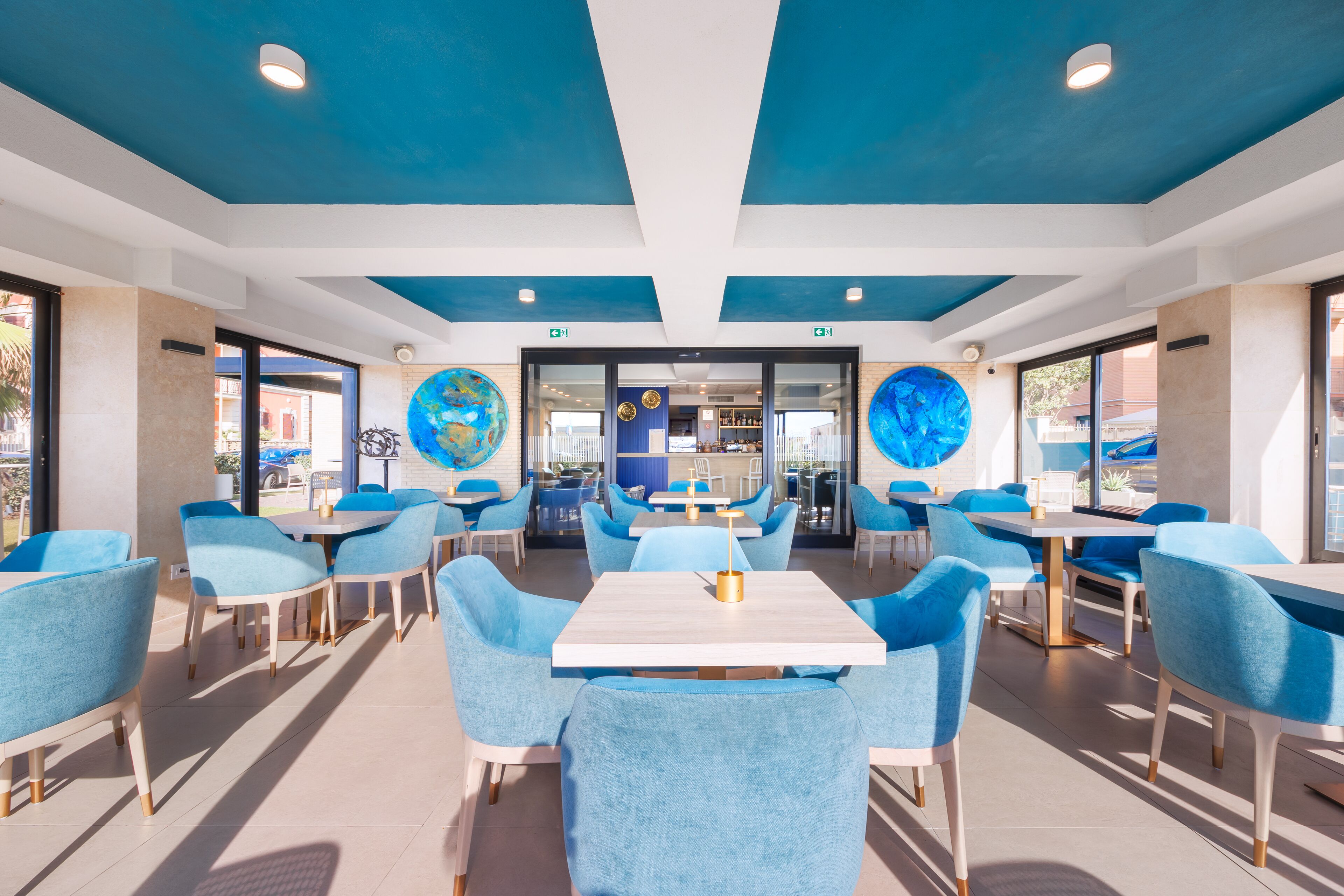 Un comedor moderno con sillas y mesas azules, grandes decoraciones de globos en el techo y vista al área exterior a través de puertas de vidrio.