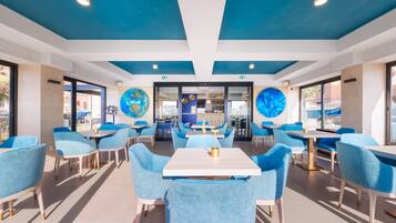 Un comedor moderno con sillas y mesas azules, grandes decoraciones de globos en el techo y vista al área exterior a través de puertas de vidrio.