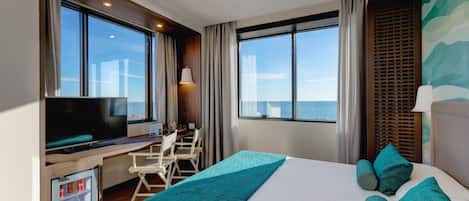 Habitación de hotel con una cama grande, un escritorio con televisor y vista al mar.
