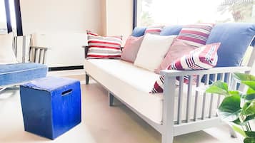 A modern living room with a white sofa, striped pillows, a blue stool, and a potted plant.