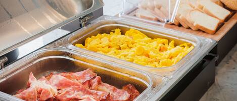 Un bufé con diversas opciones de comida, incluyendo carnes, huevos revueltos y pastelería.