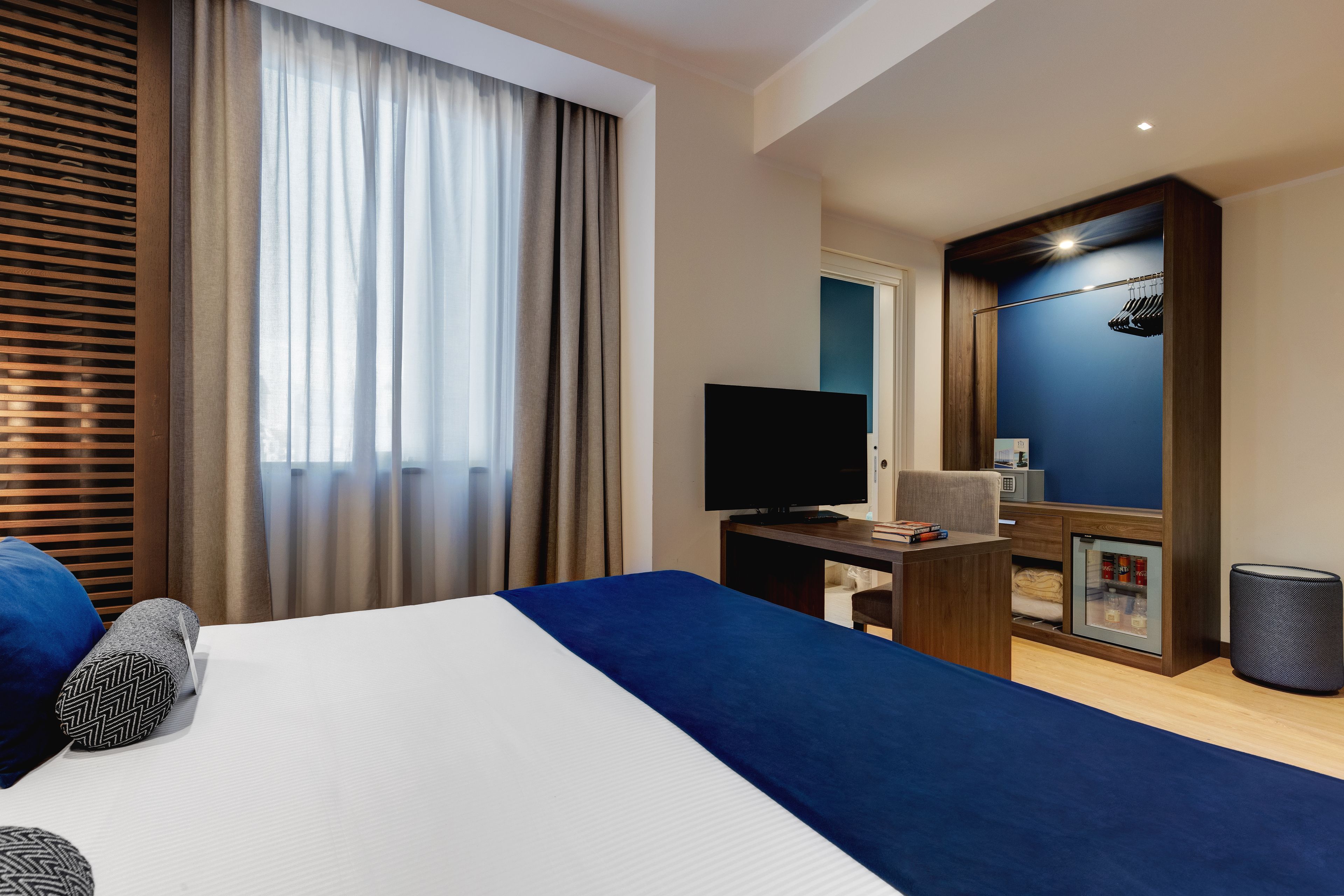 Habitación de hotel con una cama grande, un escritorio con televisor de pantalla plana, armario y un refrigerador pequeño.