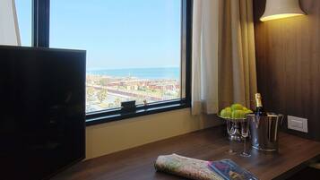 Habitación de hotel con televisión, una mesa con un mapa, una botella de champán y vistas a la ciudad y al océano.