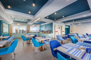 A modern dining area with blue chairs and tables, a kitchen in the background, and a blue ceiling.