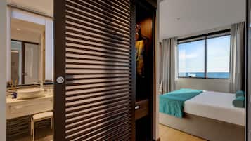 A modern hotel room with a large window, a bed, a bathroom with a sink, and a wardrobe.