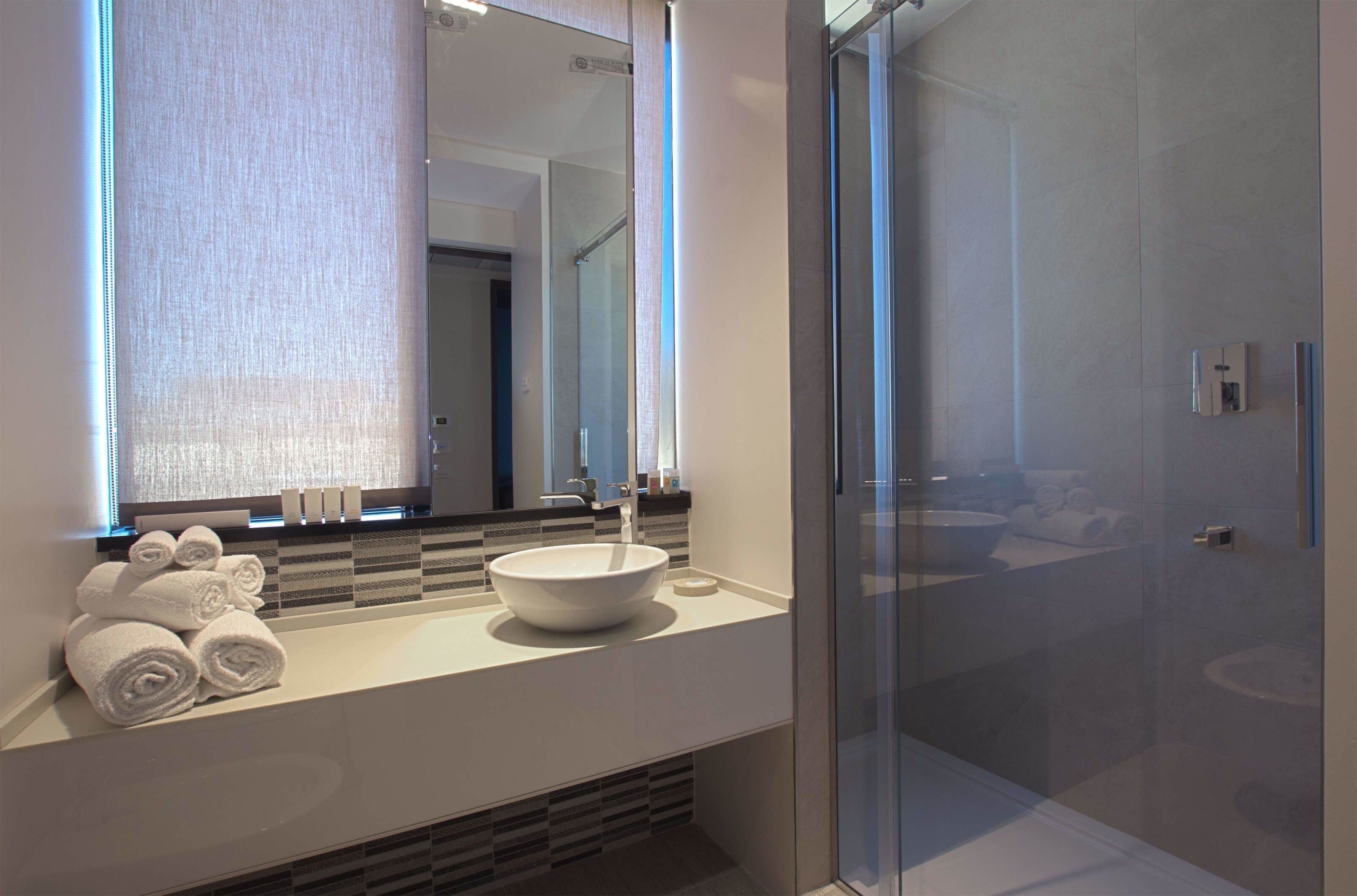 A modern bathroom with a large mirror, white sink, and glass shower enclosure.