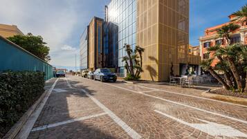 A cobblestone street lined with modern buildings, a clear sky, and parked cars.