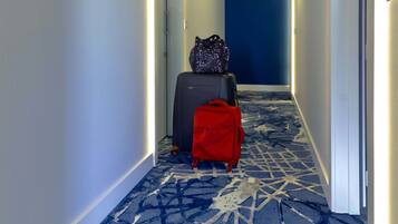 Un pasillo de hotel con alfombra estampada, una maleta roja y una maleta negra.