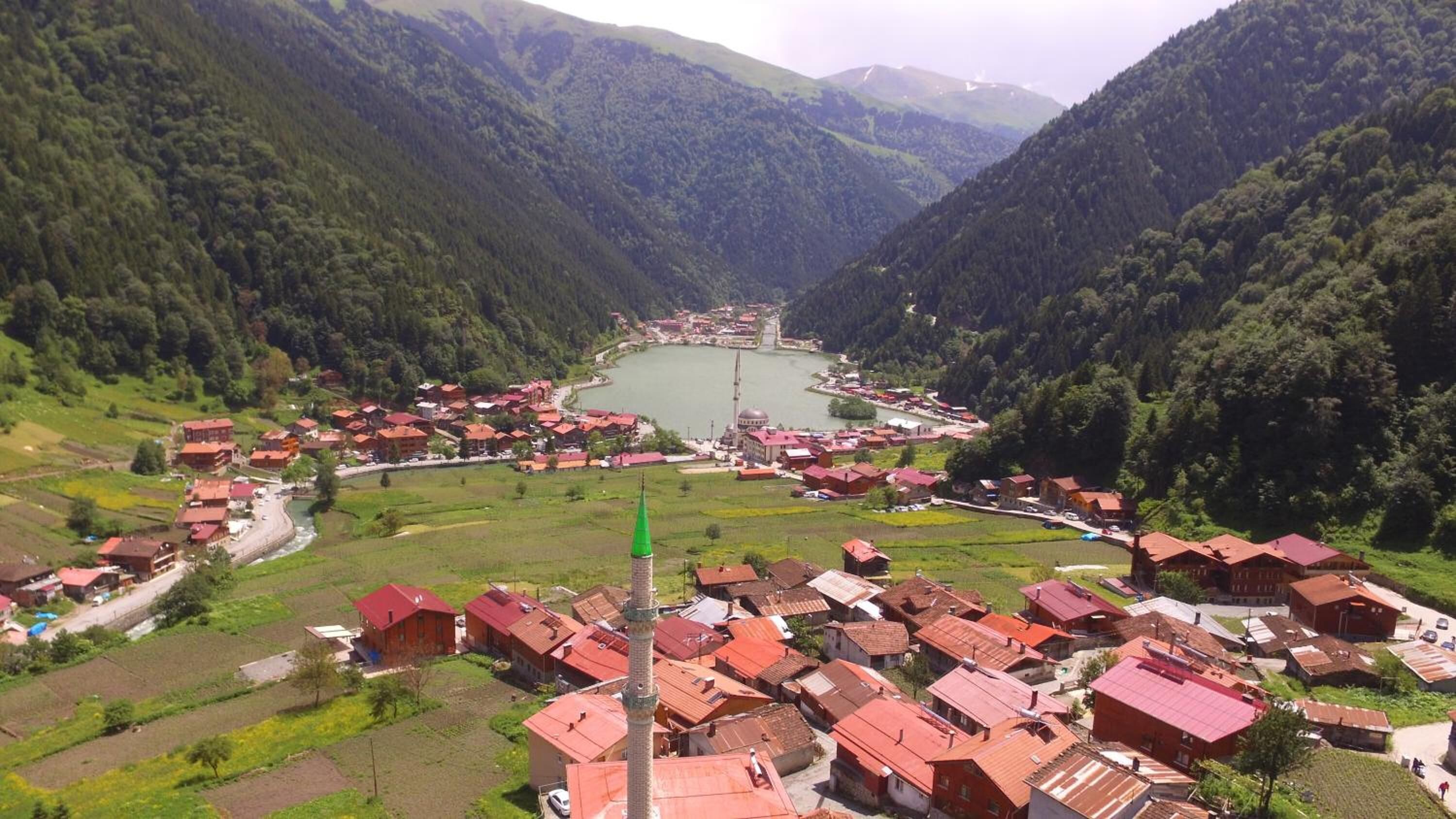 A village with red-roofed buildings, a central mosque, and a lake surrounded by mountains.