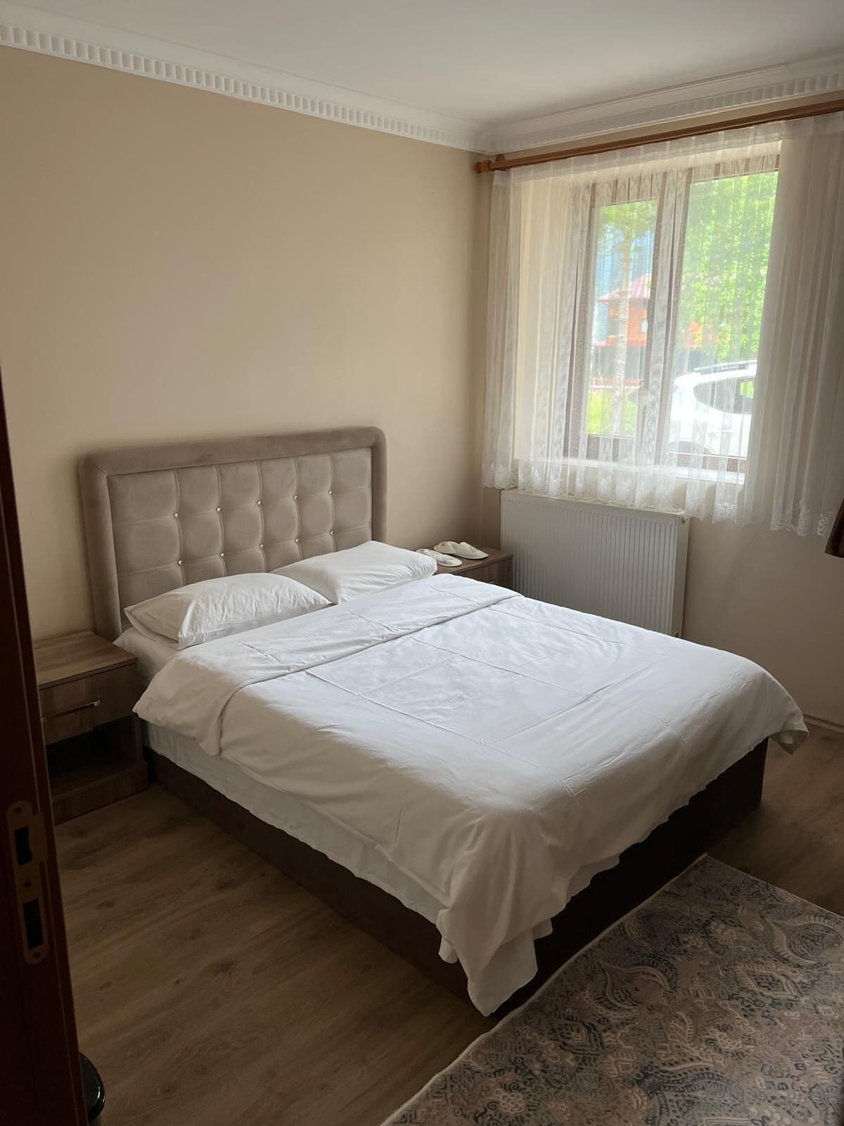 A bedroom with a bed, a bedside table, a window with curtains, and a patterned rug.