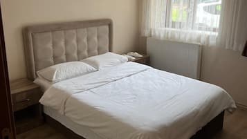 A bedroom with a bed, a bedside table, a window with curtains, and a patterned rug.