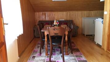 A wooden-paneled room with a dining table and chairs, a kitchen area with a refrigerator, and a patterned rug on the floor.