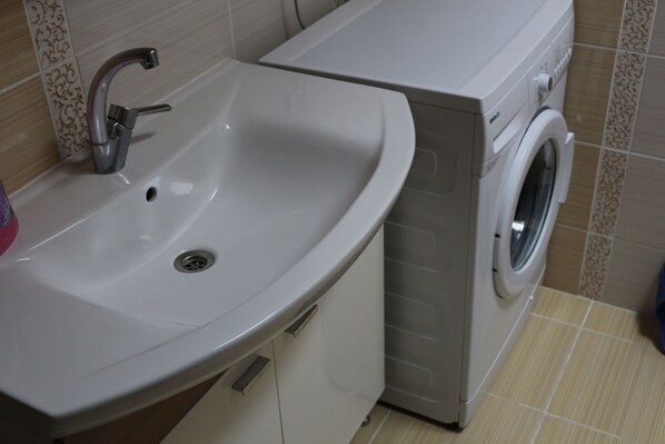 A bathroom with a sink, a washing machine, and tiled walls.
