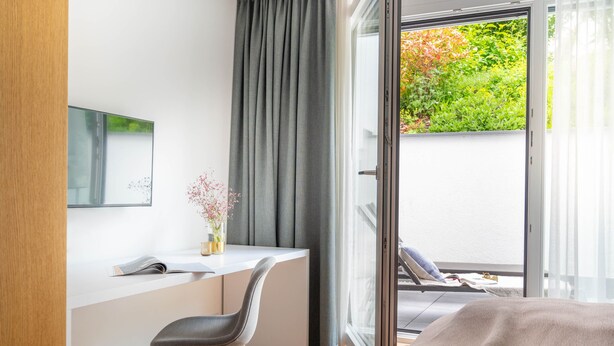 A modern bedroom with a large window, a bedside table, a chair, and a bed. - Bodensee Apartment Fischbach (Friedrichshafen)