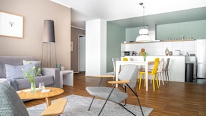 A modern living room with a grey sofa, a coffee table, and a dining area with a white table and yellow chairs. - Bodensee Apartment Fischbach (Friedrichshafen)