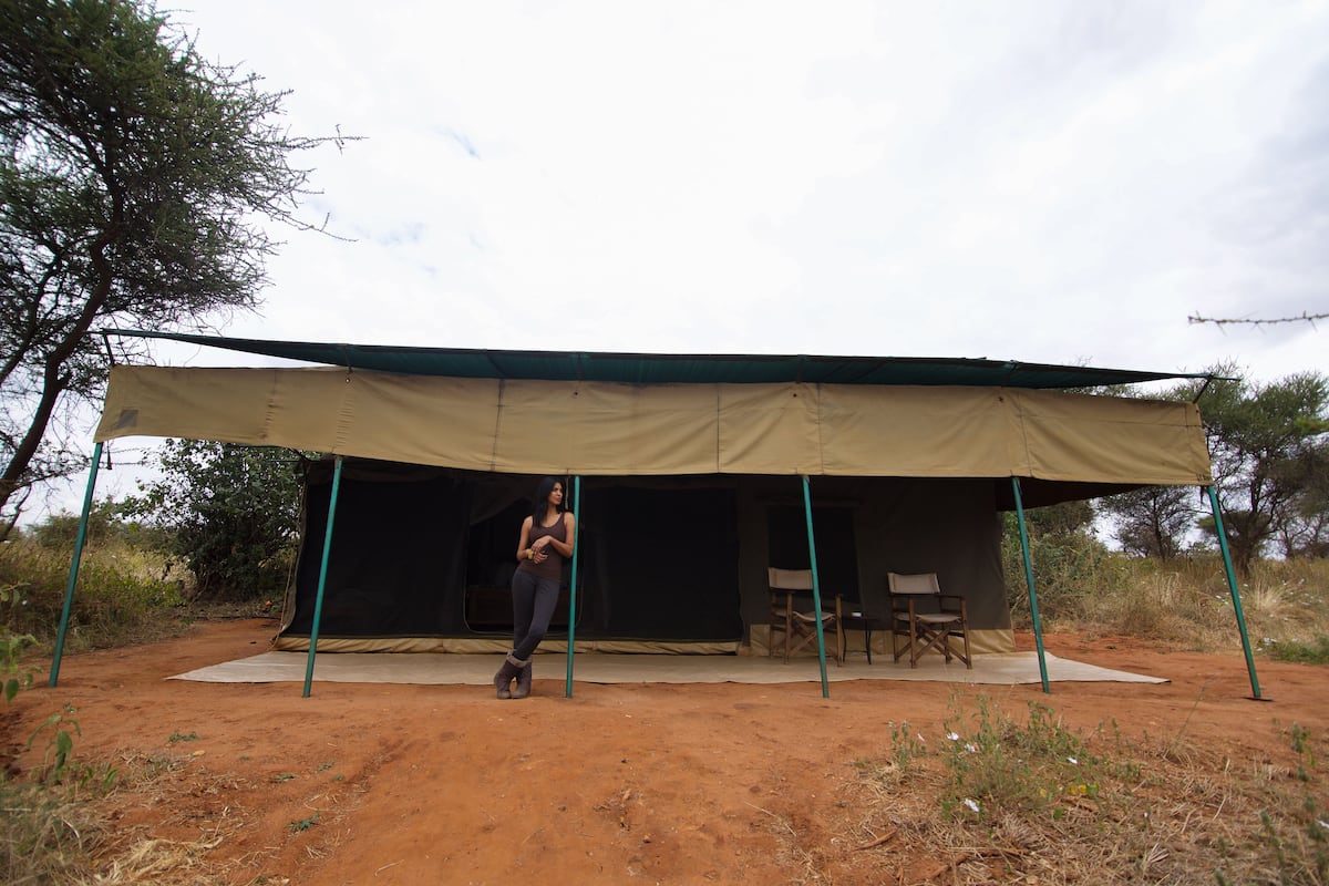 A tent with a green frame and a beige canopy, set on a dirt ground with sparse vegetation.