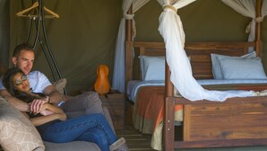 Une tente avec un lit en bois et un espace salon doté de coussins.