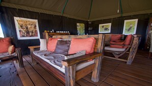 Un hébergement sous tente comprenant un canapé-lit en bois, des chaises en bois et des photographies d’animaux sauvages encadrées accrochées aux murs.