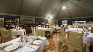 Un espace de restauration intérieur avec des tables dressées pour le repas, un bar en arrière-plan et une structure en forme de tente au-dessus.