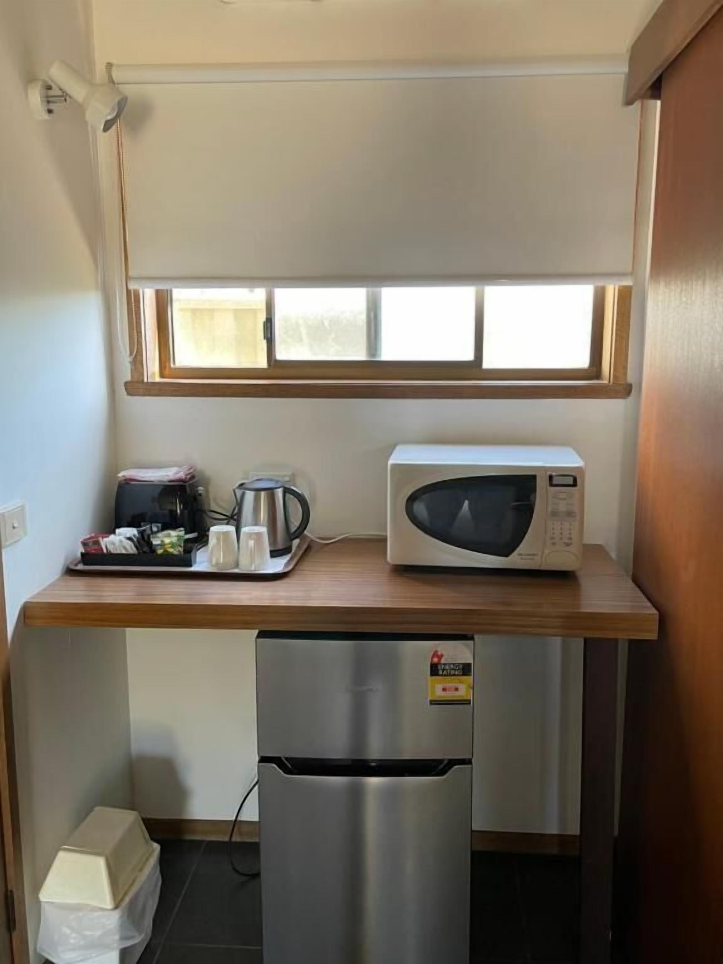 Una kitchenette compacta equipada con microondas, un refrigerador pequeño y una ventana sobre la encimera.