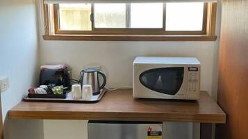 Una kitchenette compacta equipada con microondas, un refrigerador pequeño y una ventana sobre la encimera.