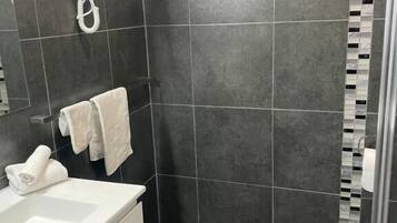 A bathroom with a white sink, dark tiles, a towel rack, and a shower area.