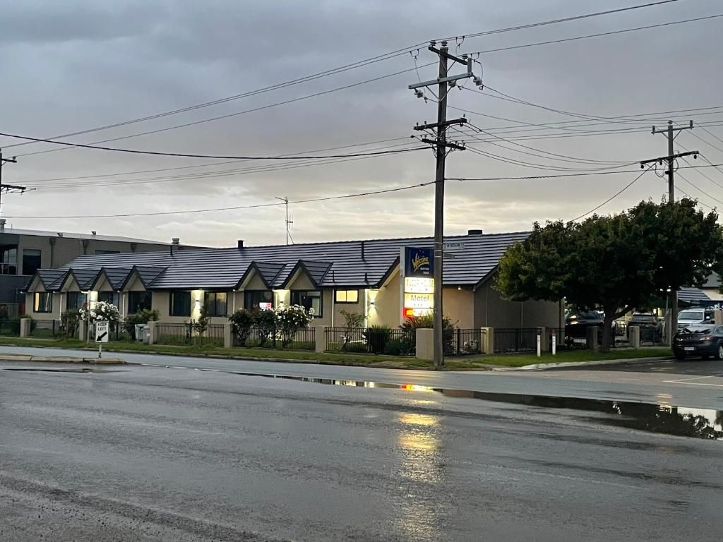 A motel with a row of single-story buildings, a parking lot, and a wet road reflecting the sky.