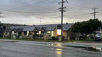 A motel with a row of single-story buildings, a parking lot, and a wet road reflecting the sky.