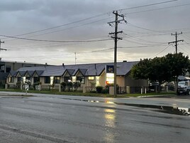 Un motel con una hilera de edificios de una planta, un estacionamiento y un camino mojado que refleja el cielo.