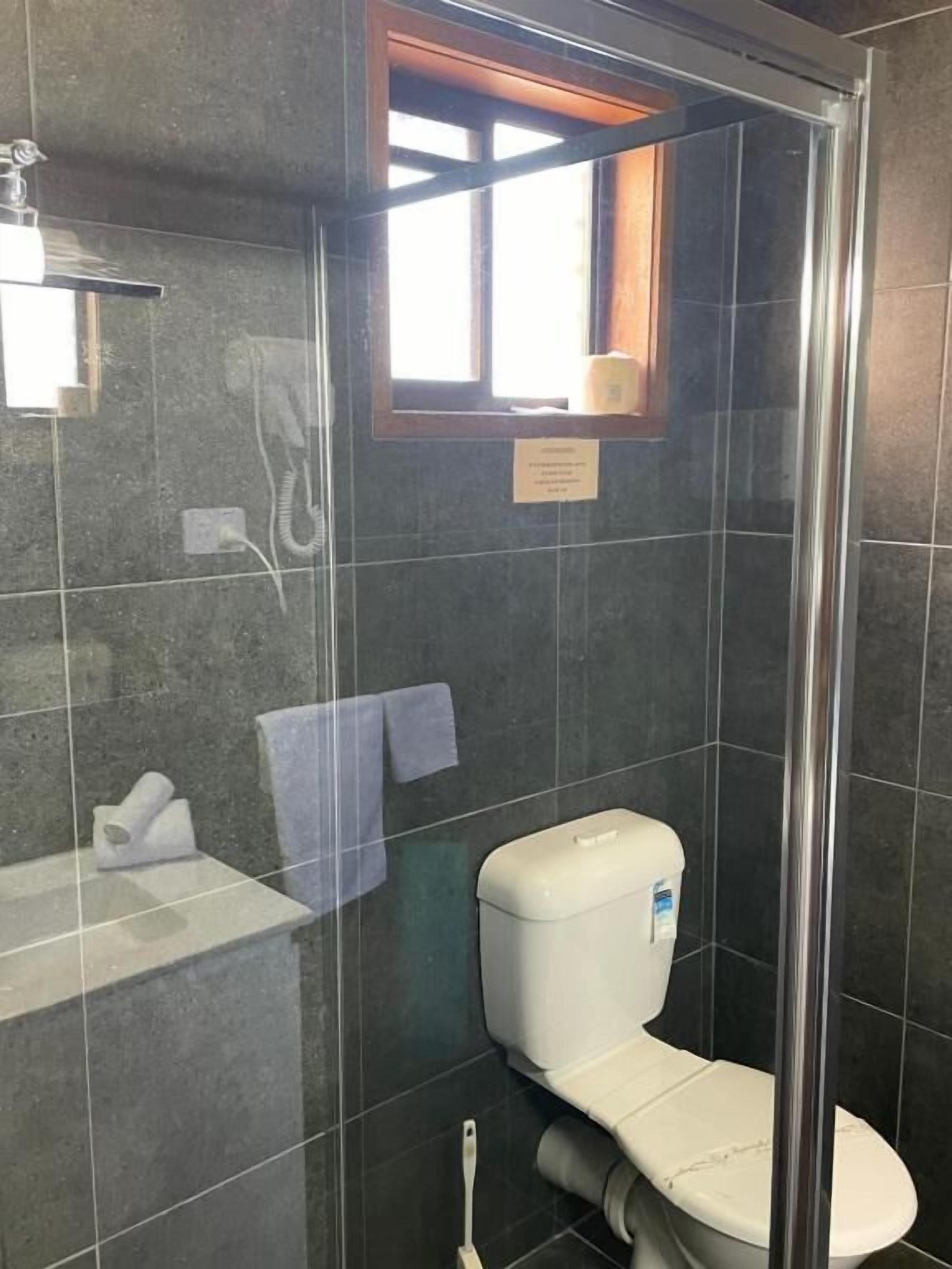 Un baño con ducha envuelta en vidrio, inodoro, lavamanos y ventana.