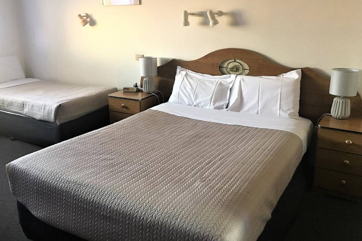 Habitación de hotel con dos camas, cada una con cabecero de madera, una mesita de noche con lámpara y una obra de arte colgada en la pared.