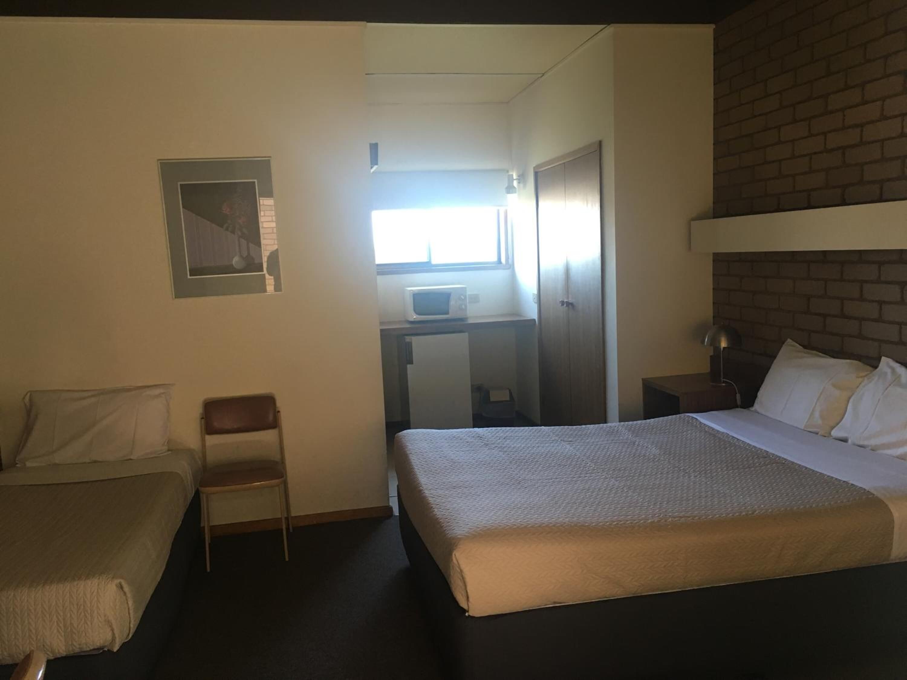 A hotel room with two beds, a desk with a computer, a chair, and a window.