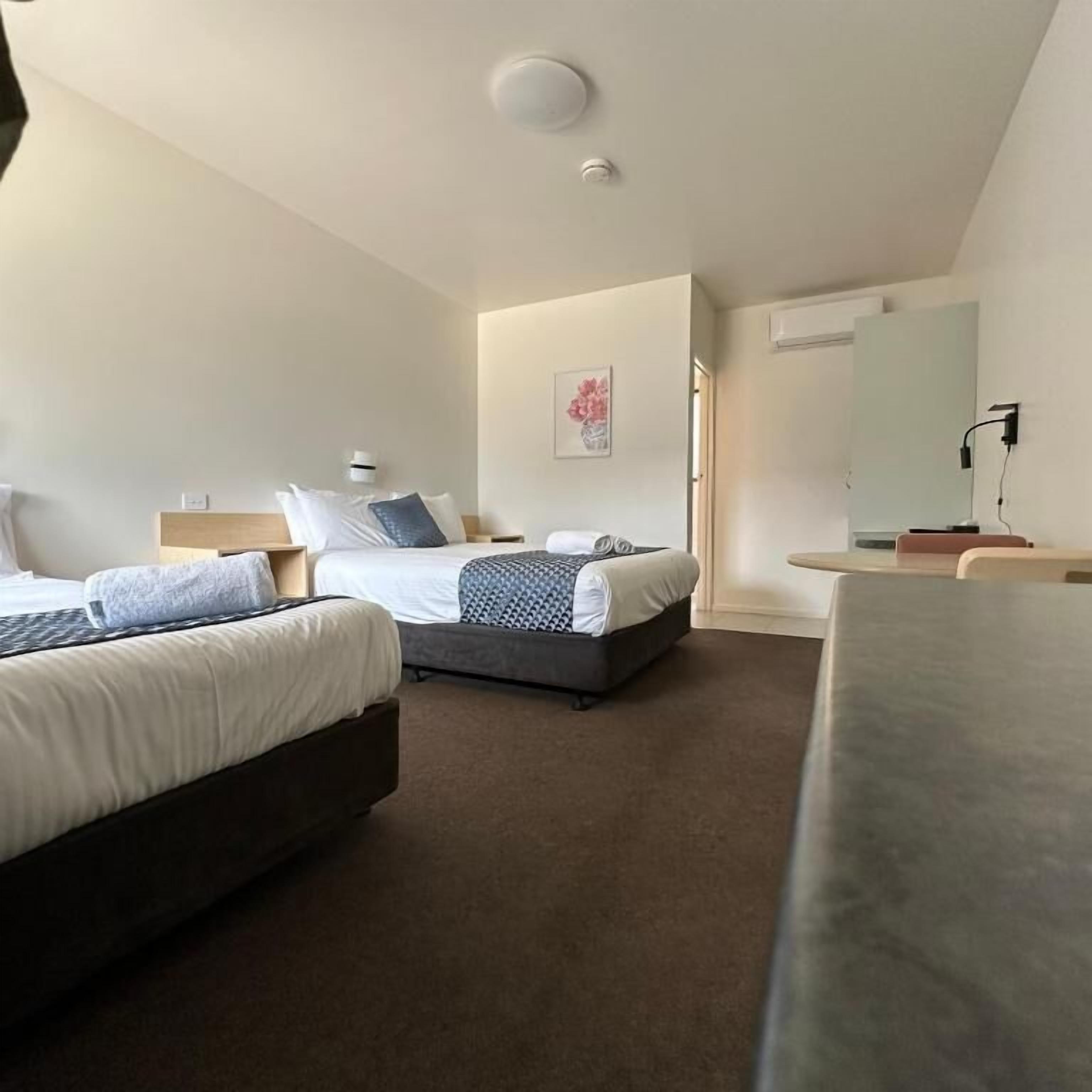 Habitación de hotel con dos camas, un escritorio, una silla, un espejo y una ventana.