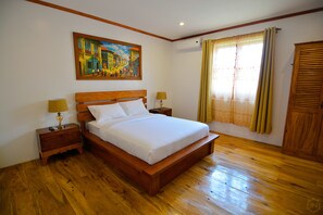 A neatly made bed in a room with wooden floors, a painting on the wall, and a window with curtains. - Casa Simeon (Bacacay)