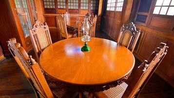 A wooden dining table surrounded by ornate chairs in a room with wooden paneled walls and large windows.