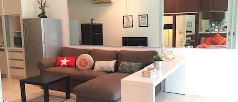 A modern living room with a sectional sofa, a small coffee table, and a white console table. There is a kitchen area visible through an open door.