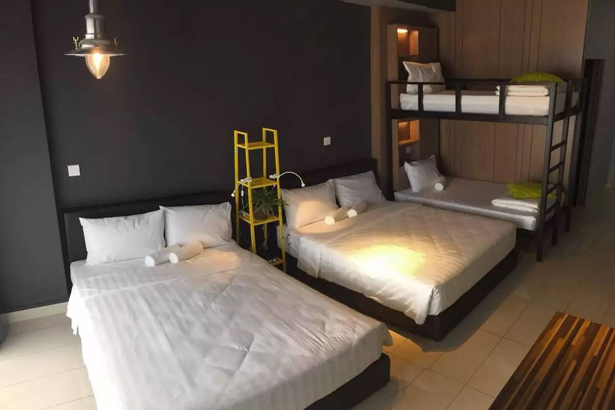 Une chambre d’hôtel avec deux lits simples, un petit bureau et un lit superposé dans un coin.
