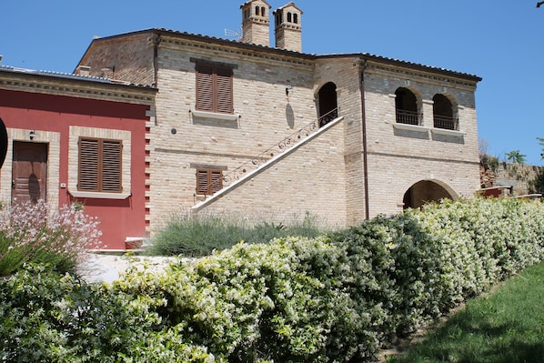A historic building with a stone facade, a staircase leading to an upper level, and a red building adjacent to it.