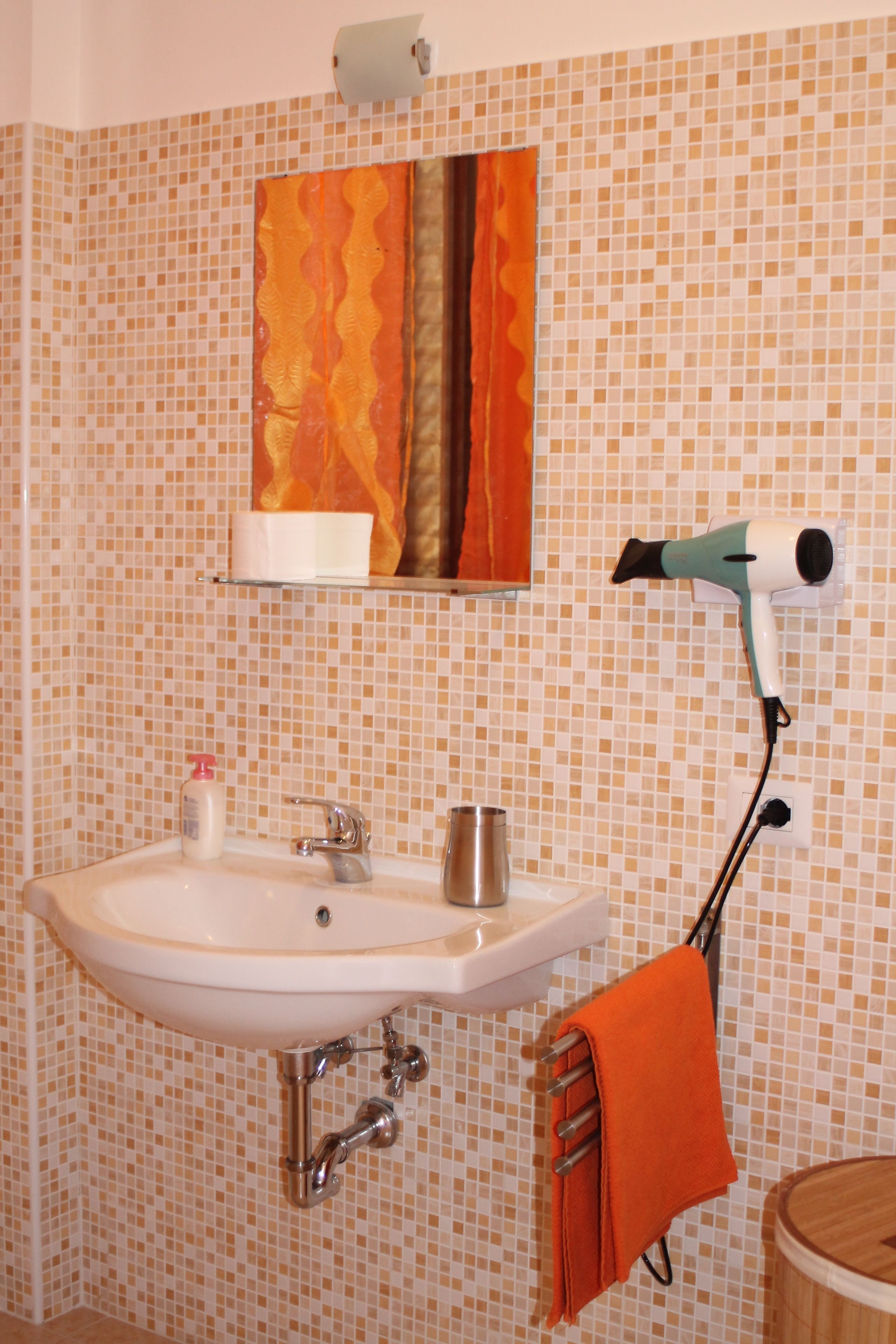 A bathroom with a sink, a towel rack, a hairdryer, and a mirror with a decorative tile backsplash.