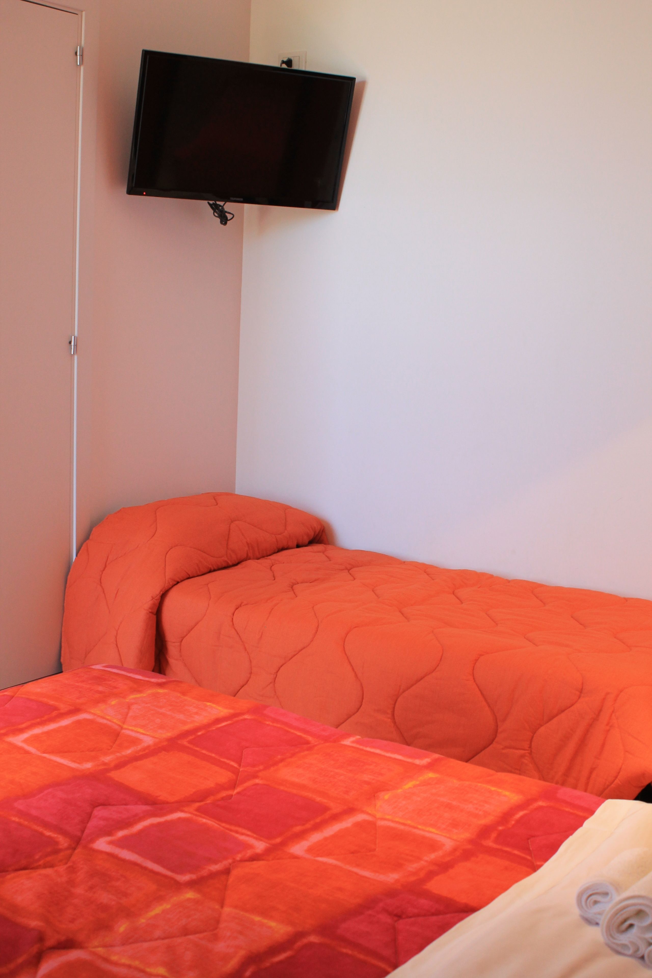 Ein Schlafzimmer mit einem Bett, einem an der Wand montierten Fernseher und einer Tür.