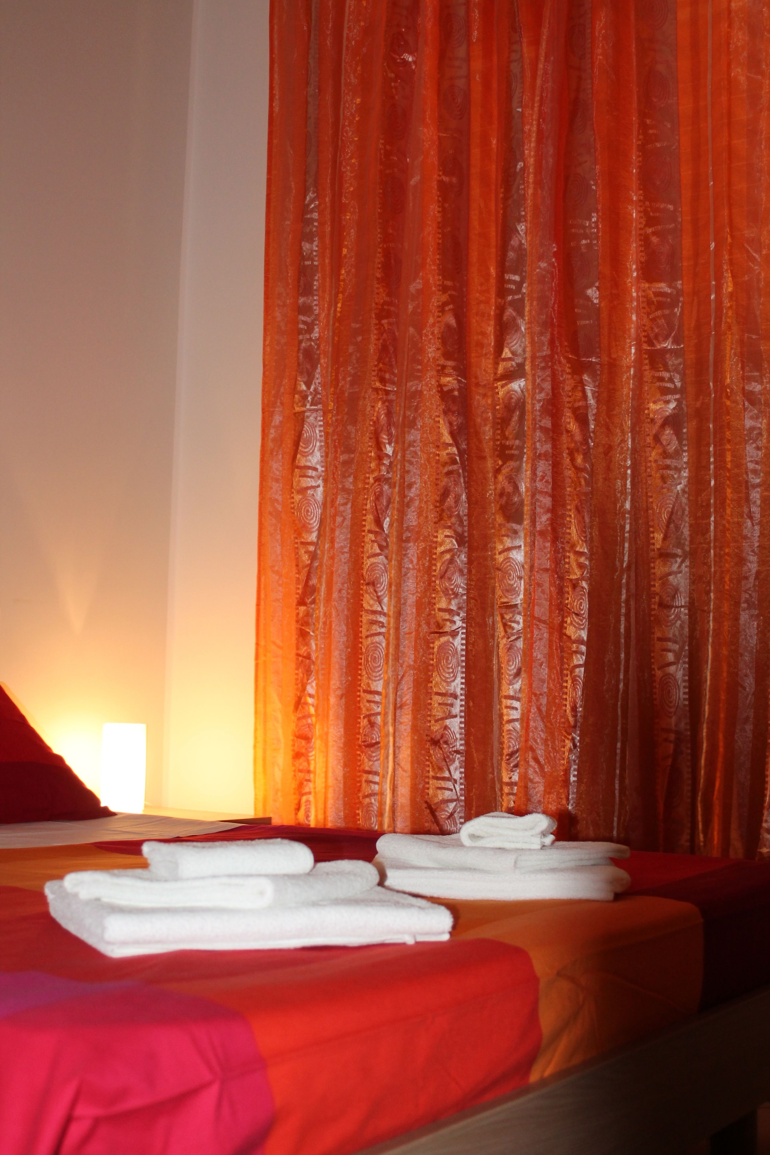 Una camera d'albergo con un letto, biancheria rossa e una tenda con motivo paisley.