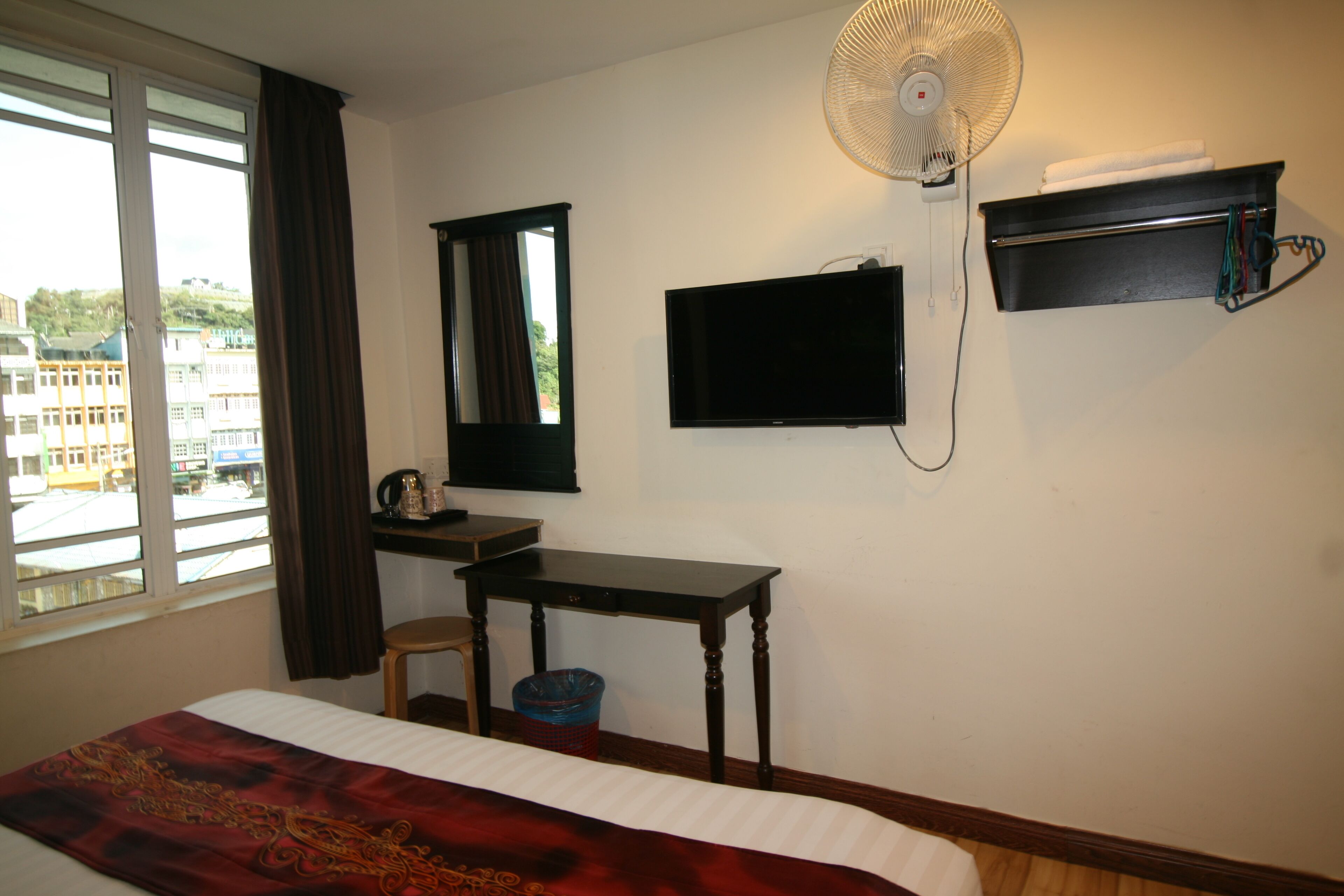 A hotel room with a bed, a desk, a television, a fan, and a window with curtains.