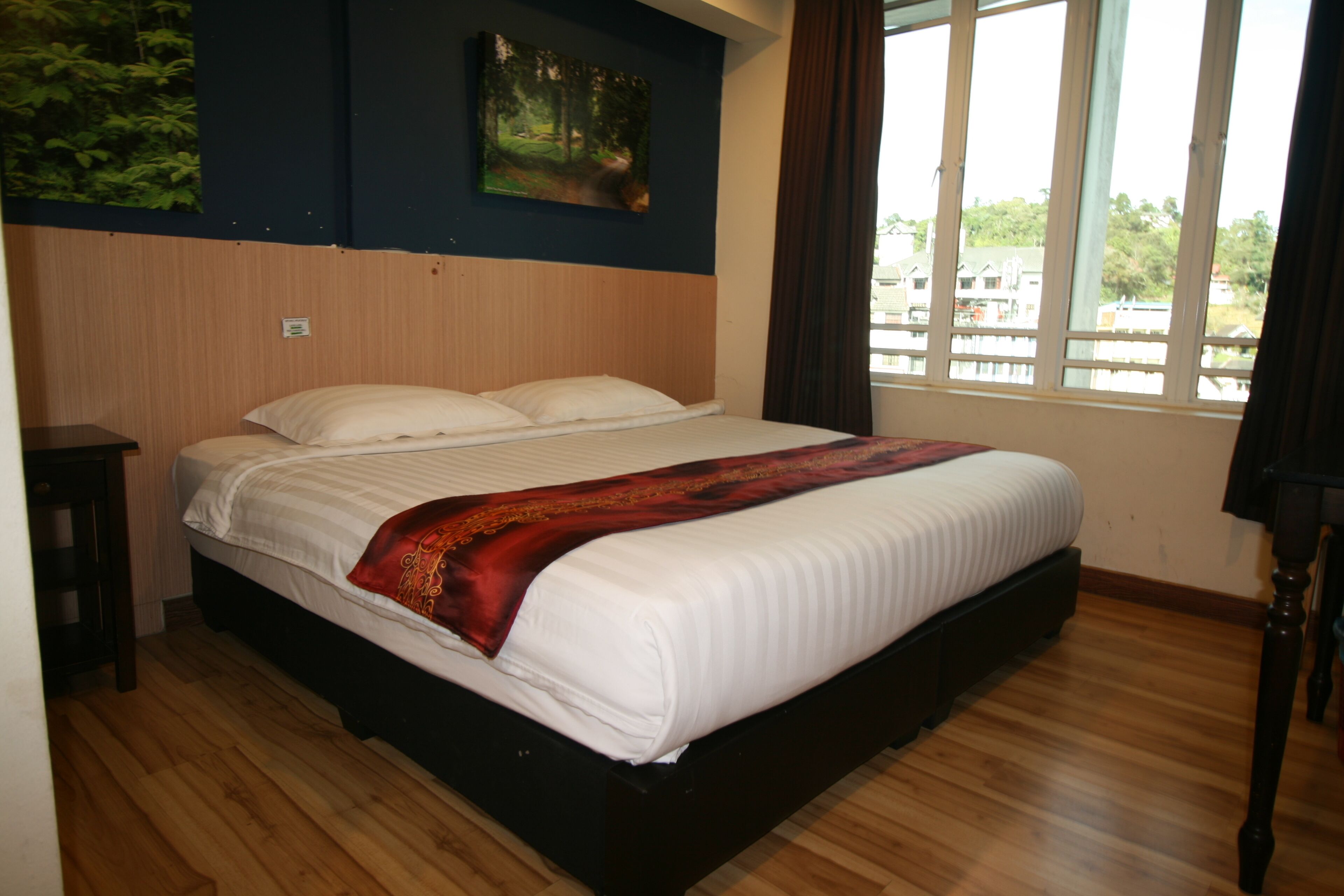 A bedroom with a large bed, wooden flooring, a window with curtains, and a painting on the wall.