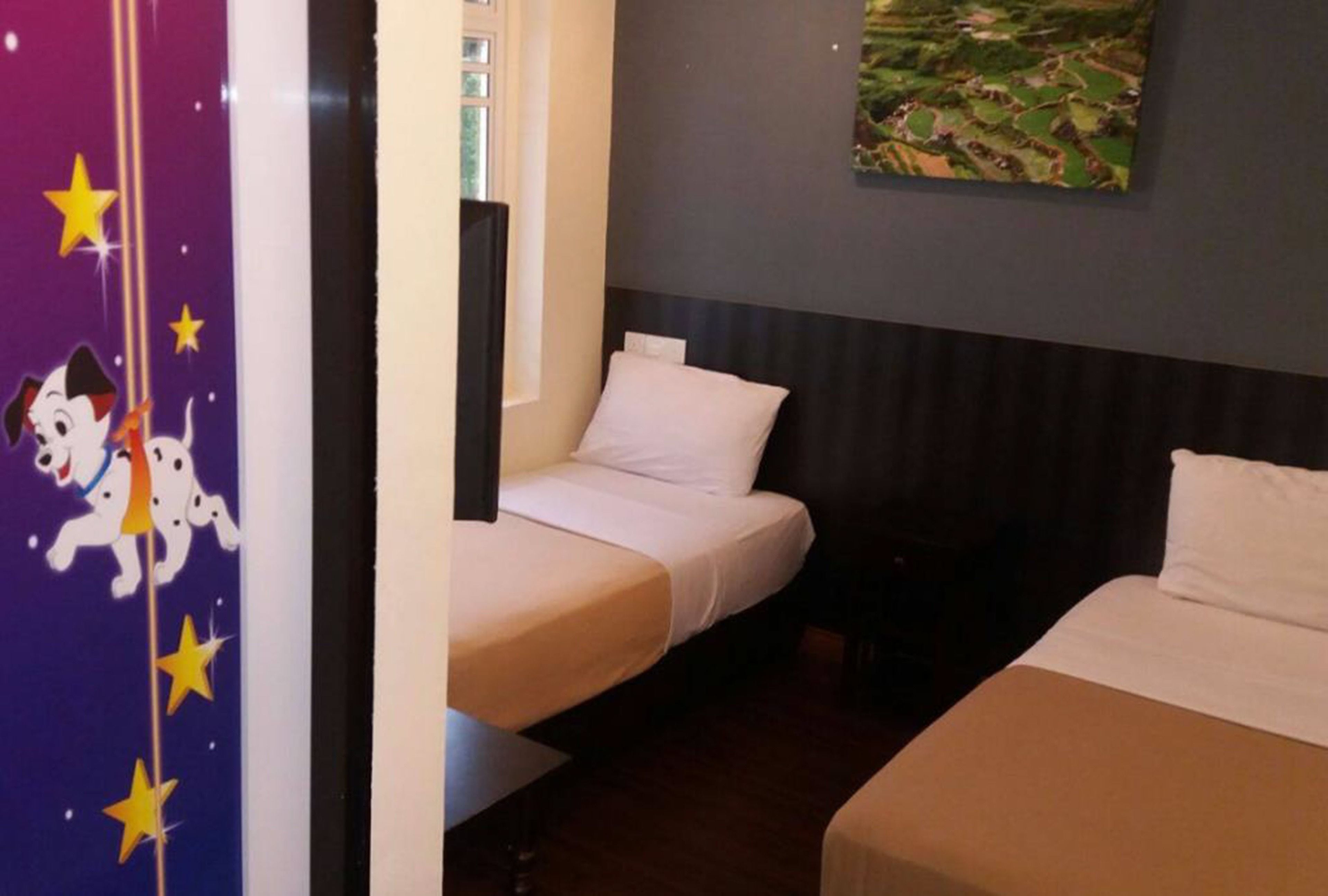 A hotel room with two single beds, a nightstand, a wall-mounted painting, and a door with a star-themed design.