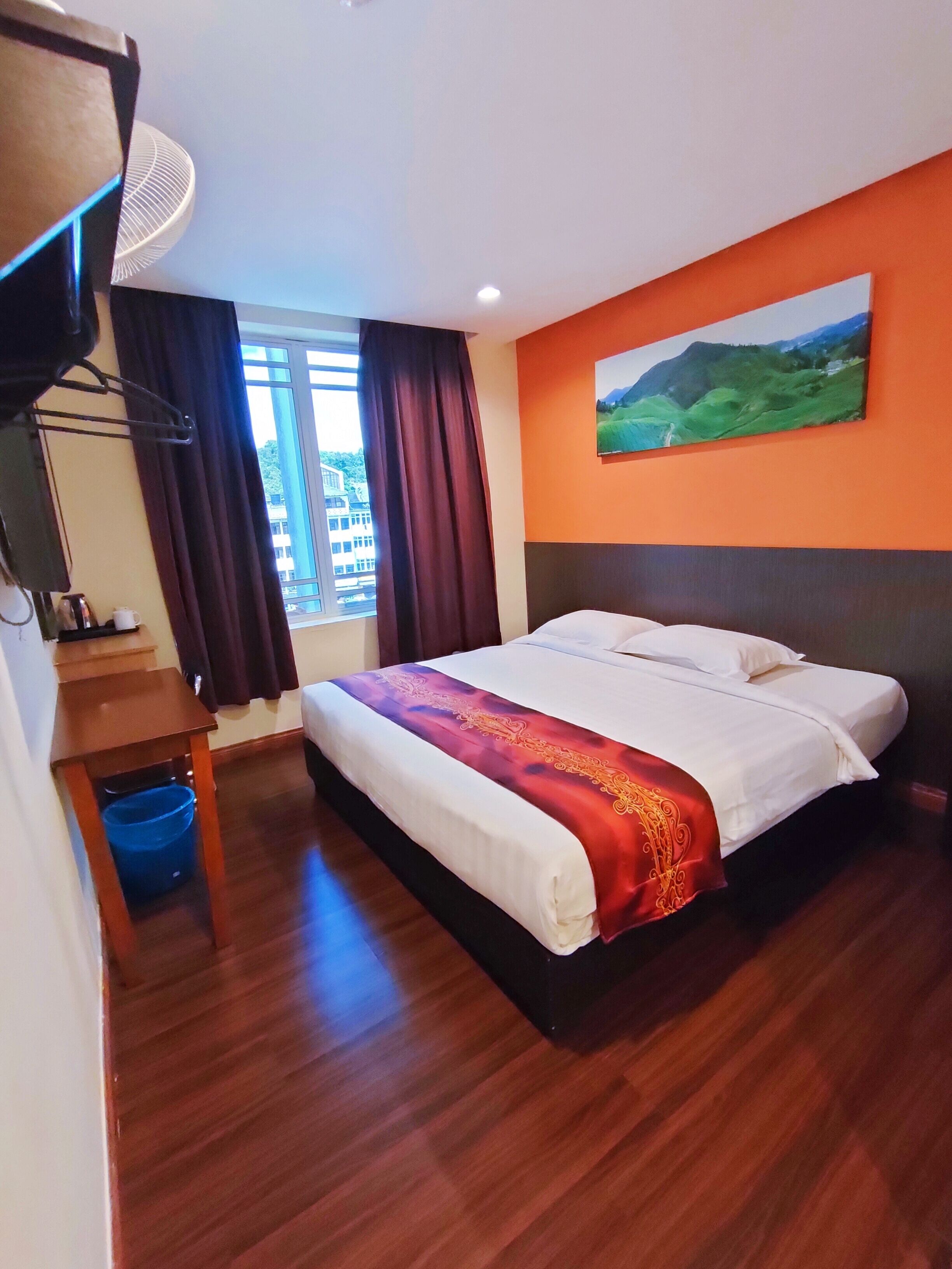 A hotel room with a large bed, a wooden floor, a painting on the wall, and a window with curtains.