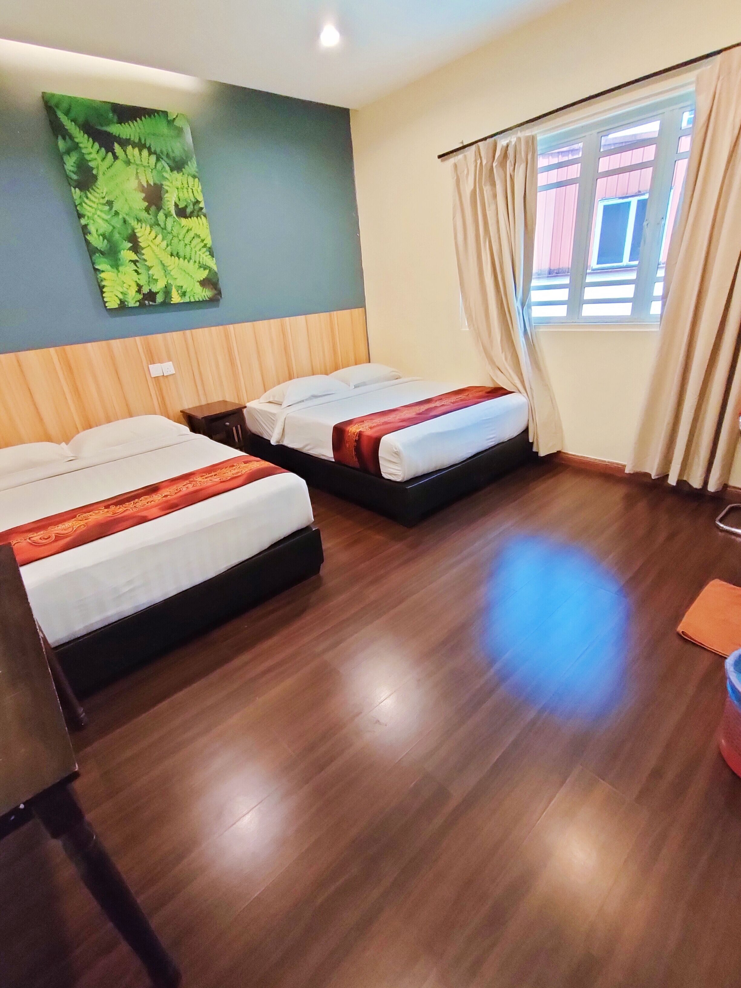 Habitación de hotel con dos camas, suelo de madera, ventana con cortinas y una obra de arte con hojas verdes en la pared.