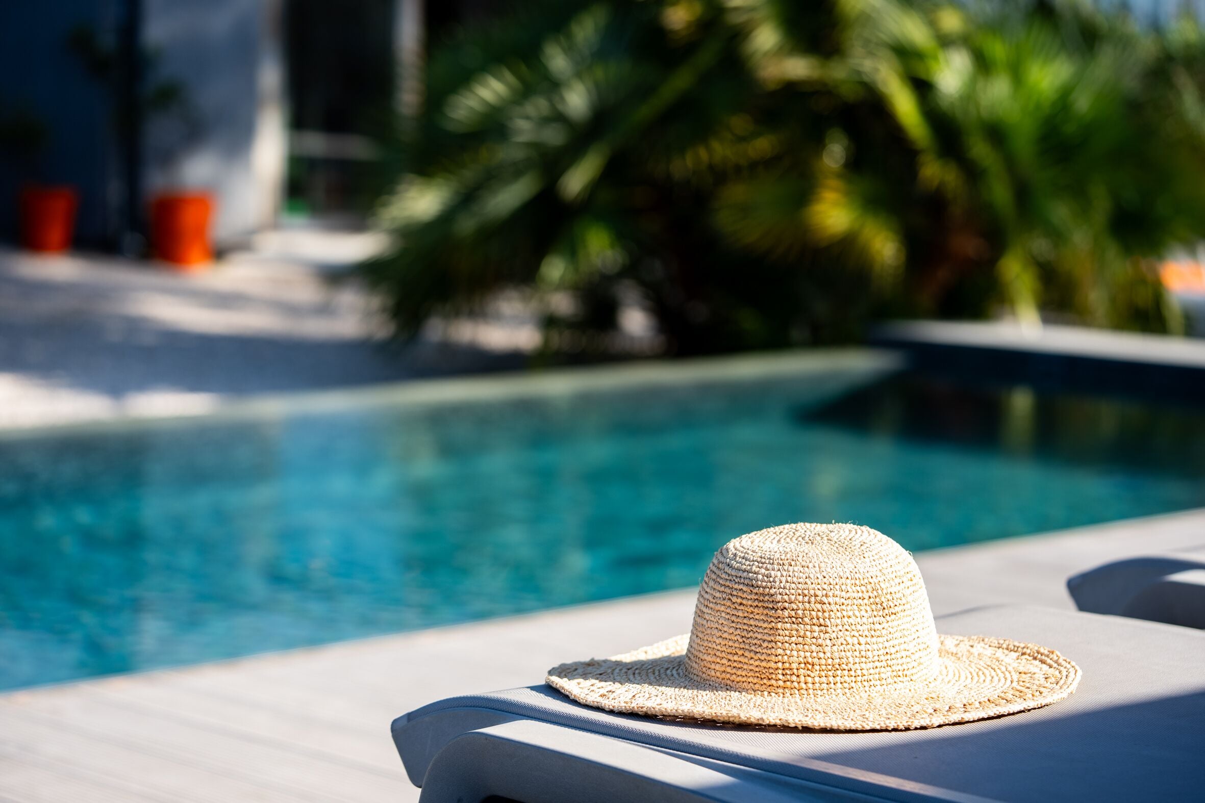 A straw hat on a lounge chair by a poolside.