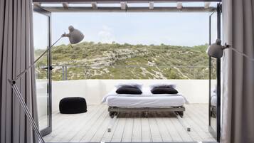 Ein Balkon mit einem Bett, zwei Lampen und Blick auf eine gebirgige Landschaft.