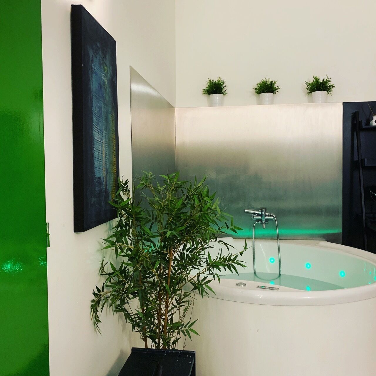 A modern bathroom with a large bathtub, a green wall, and a mirror.